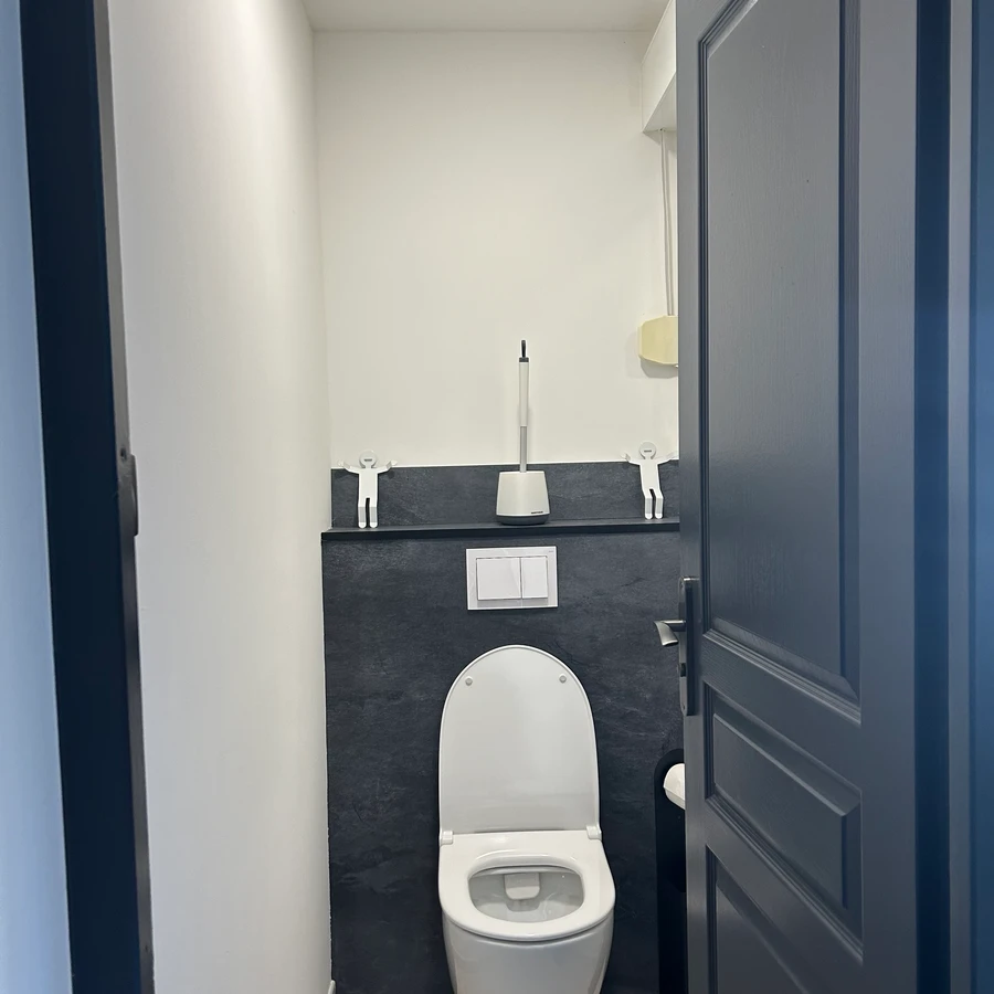 Petit WC moderne avec toilettes blanches, lavabo gris anthracite et miroir, carrelage noir et blanc, porte grise